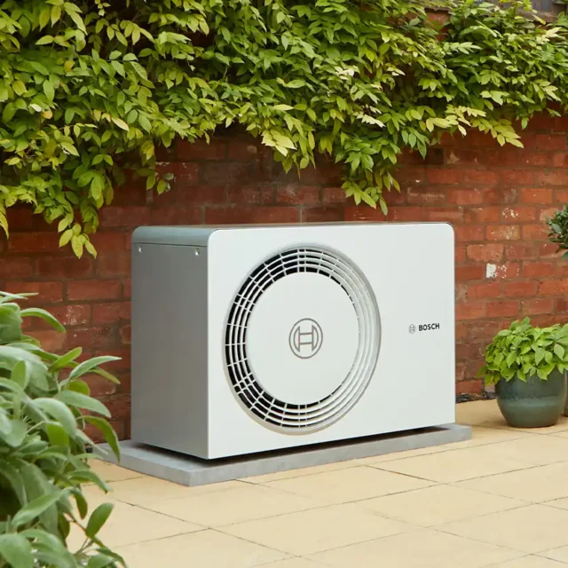 Photo of a heat pump installation in a garden against a wall - Heat Pump Installations
